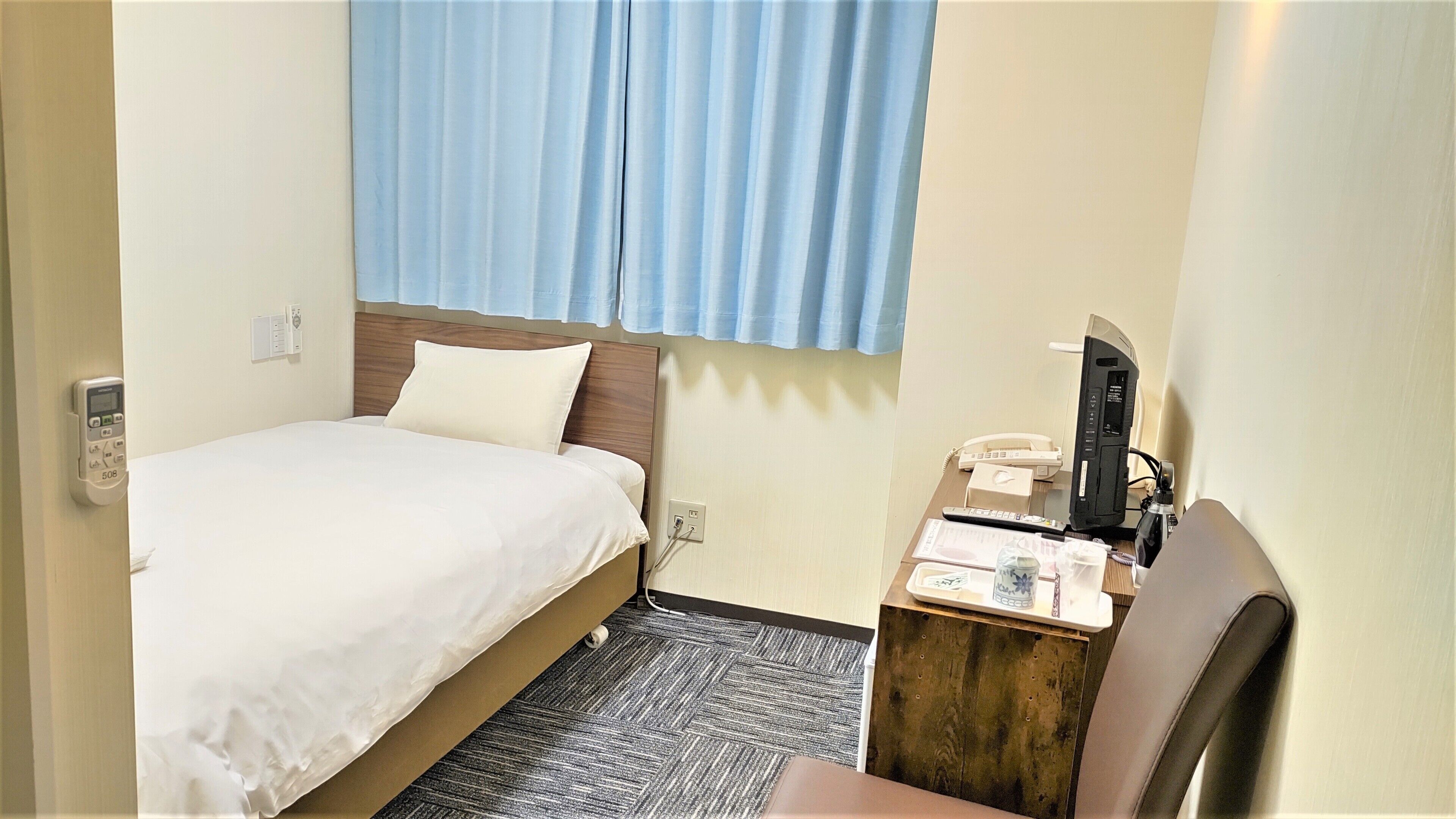 A hotel room with a bed, a desk with a telephone, and a window with curtains.