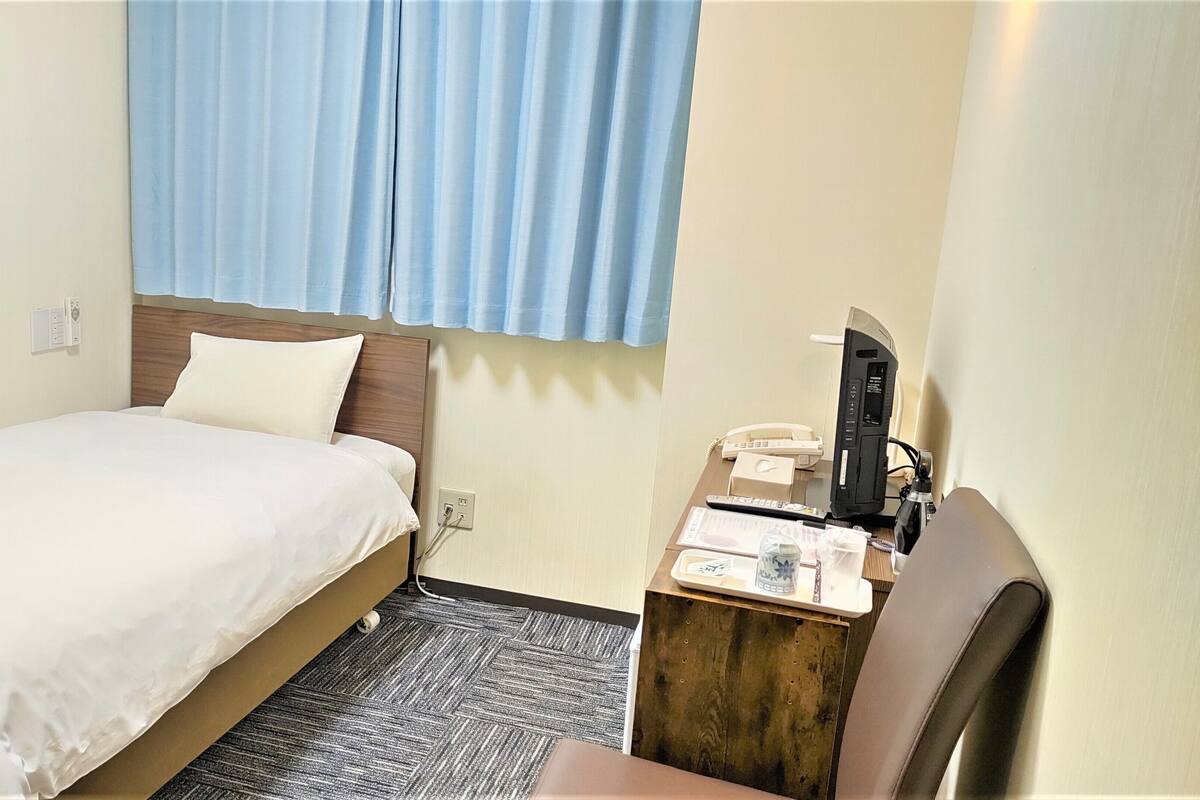 Une chambre d’hôtel avec un lit, un bureau avec un téléphone et une fenêtre avec des rideaux.