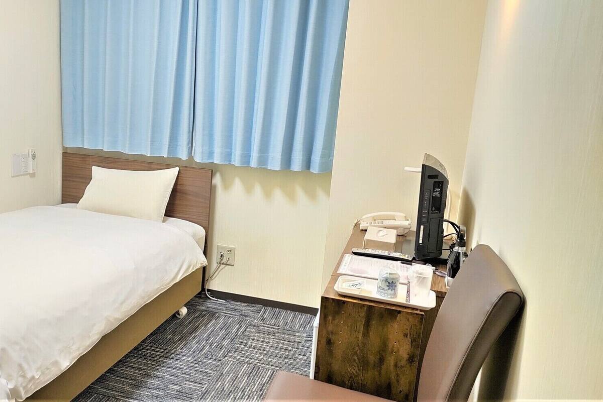 Une chambre d’hôtel avec un lit, un bureau avec un téléphone et une fenêtre avec des rideaux.