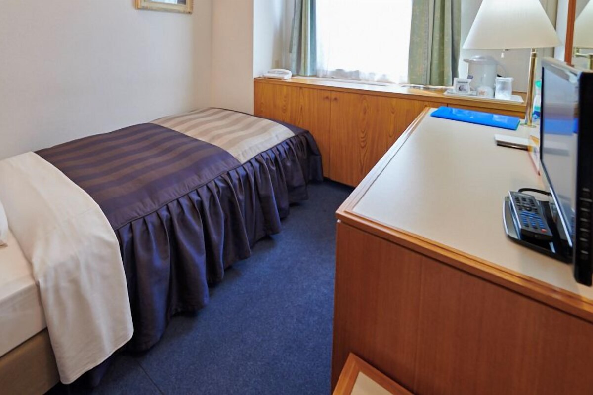 A hotel room with a bed, a desk, a telephone, and a window with curtains.