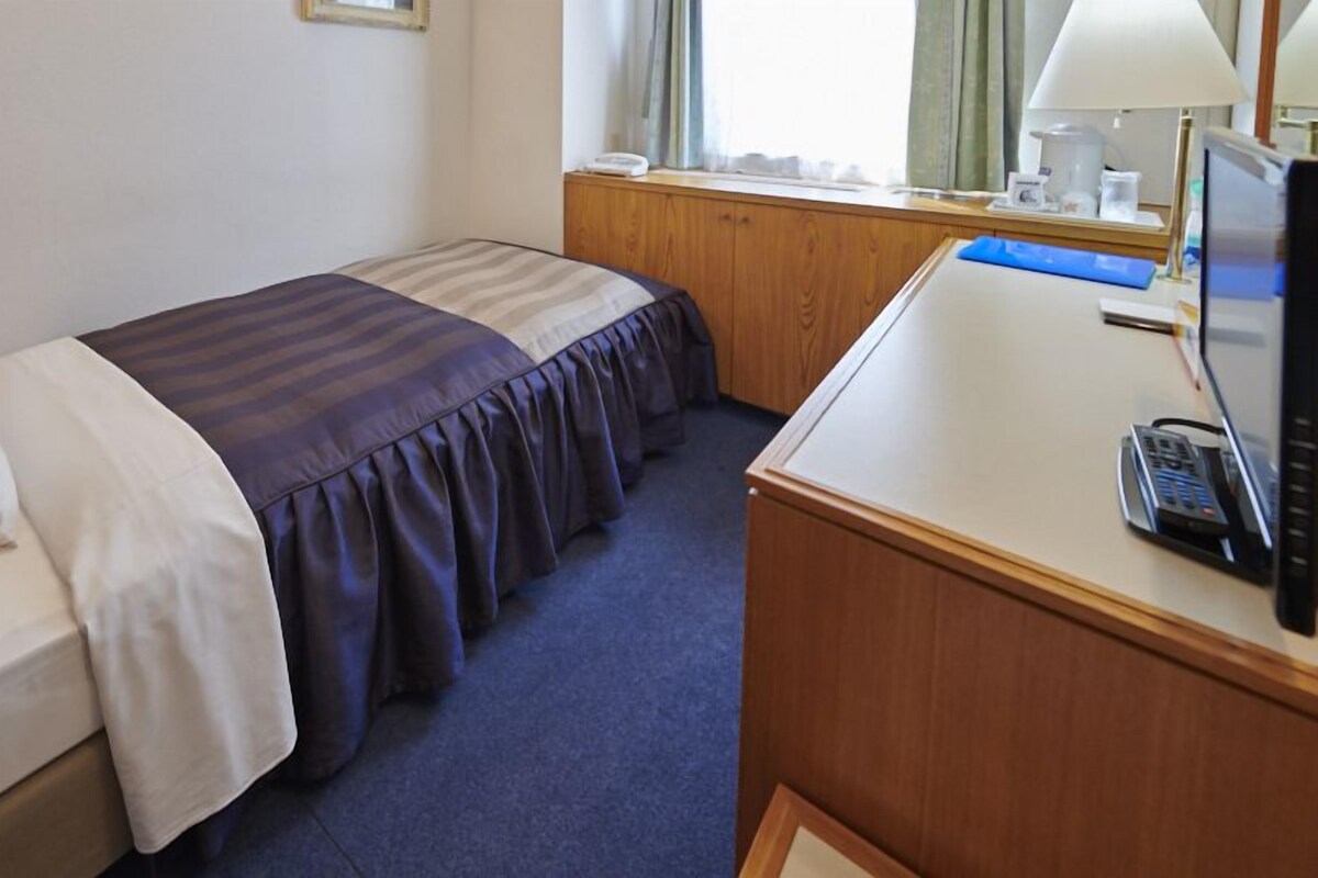 A hotel room with a bed, a desk, a telephone, and a window with curtains.