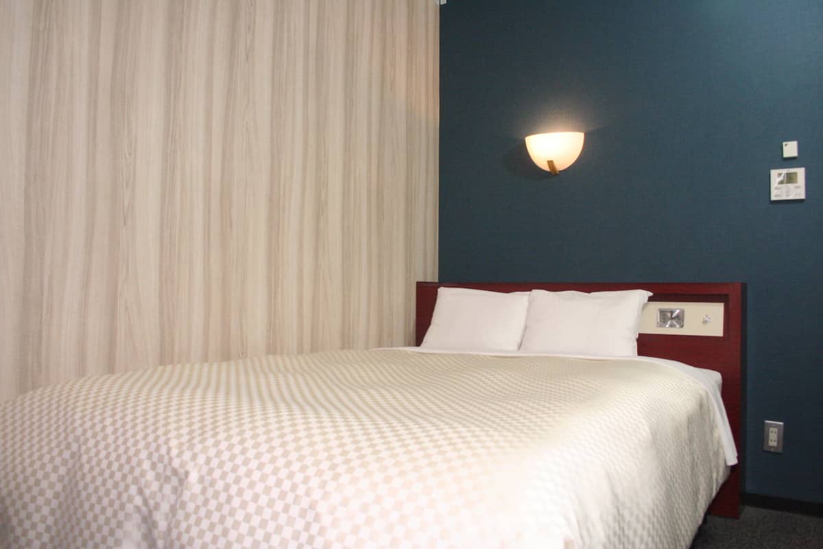 A hotel room with a bed, a wall-mounted light, and a window with curtains.