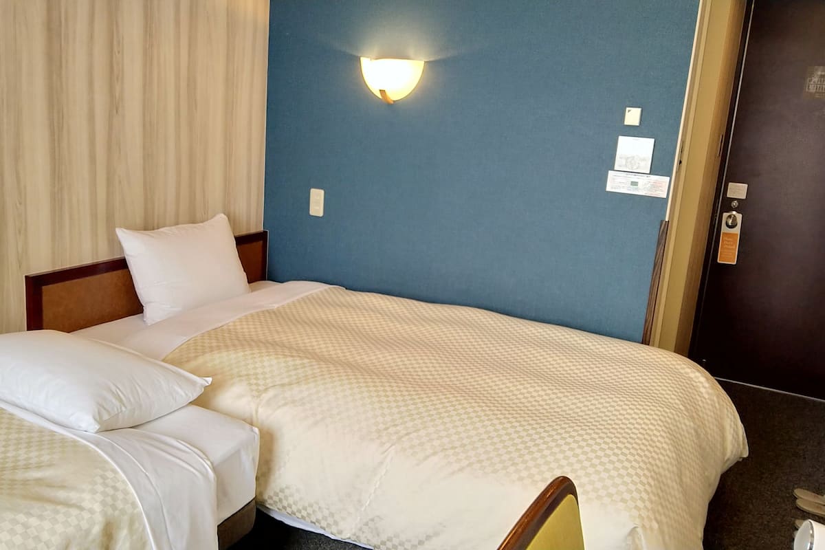 A hotel room with a bed, a nightstand, a wall-mounted light, and a door.
