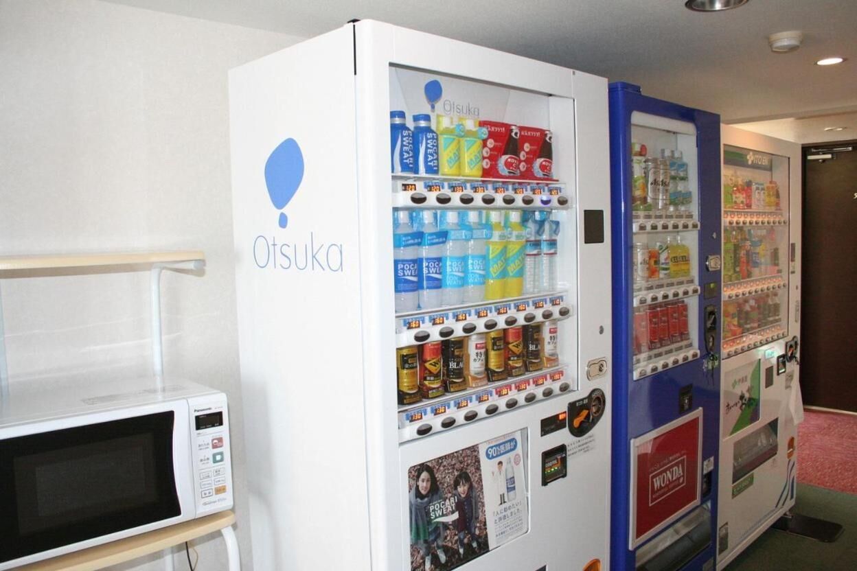 A vending machine with a variety of beverages and snacks, and a microwave on a table.