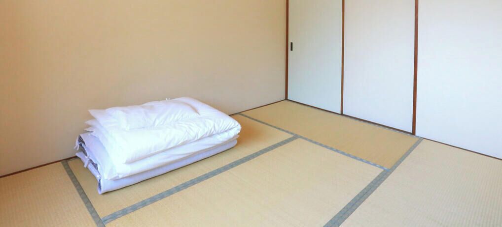 A room with tatami flooring, a neatly folded white bed, and a traditional sliding door.
