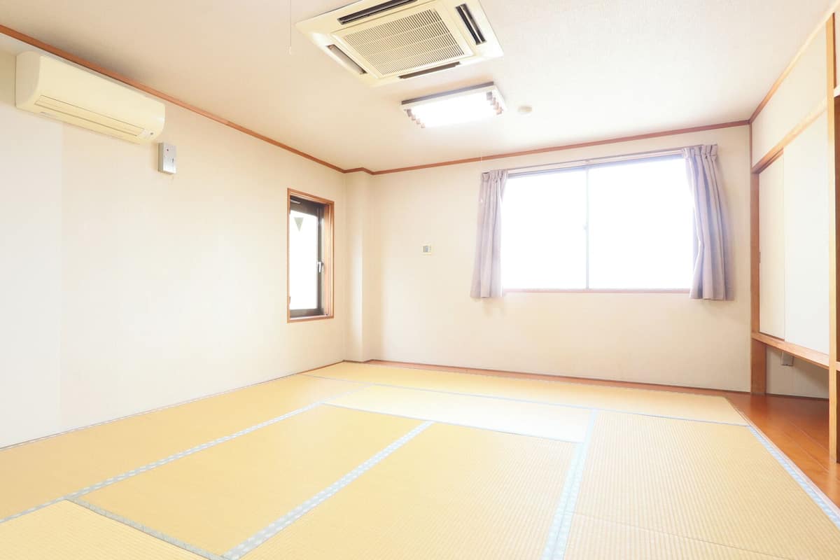 A room with tatami flooring, a window with curtains, and an air conditioning unit.