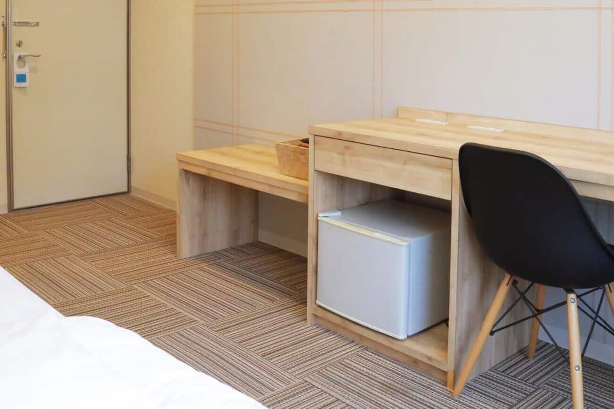 Ein Hotelzimmer mit Bett, Schreibtisch mit Stuhl, einer kleinen Ablage und einer Tür mit Schloss.