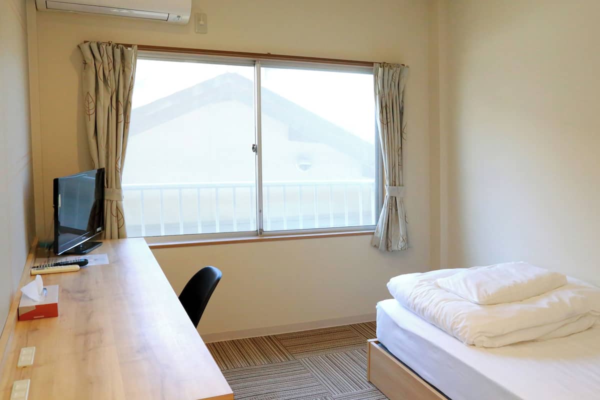 Ein Hotelzimmer mit einem Bett, einem Schreibtisch mit Computer und einem Fenster mit Vorhängen.
