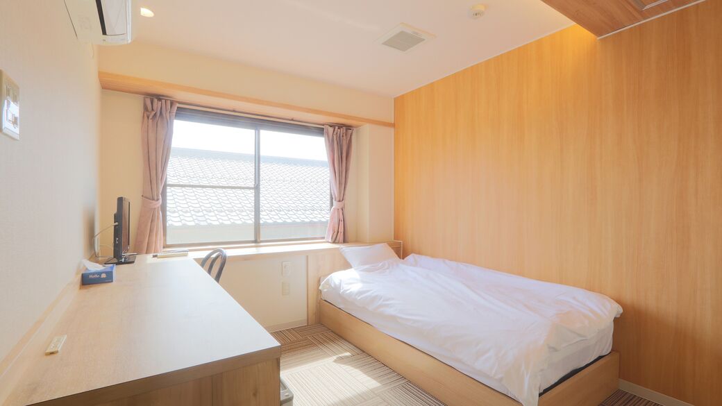 A hotel room with a bed, a desk, a window with curtains, and a view of the sea.