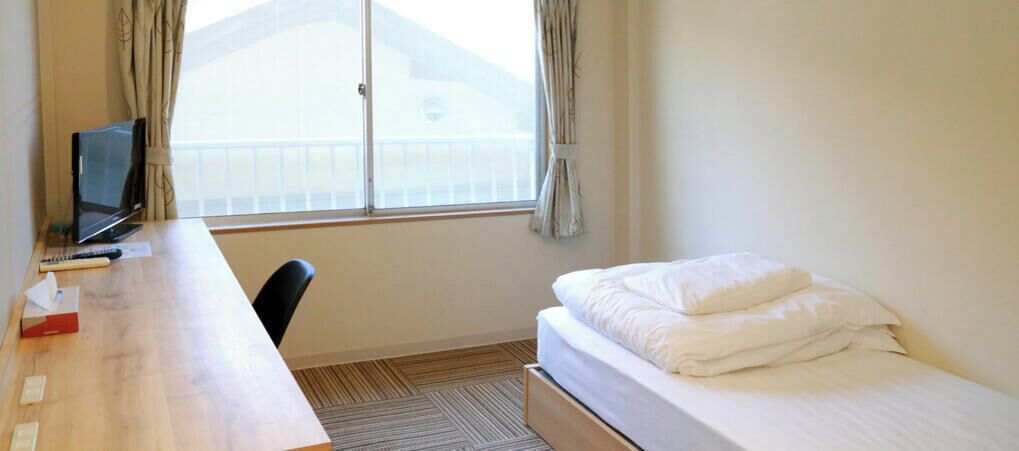 A hotel room with a bed, a desk, a chair, a TV, and a window with curtains.