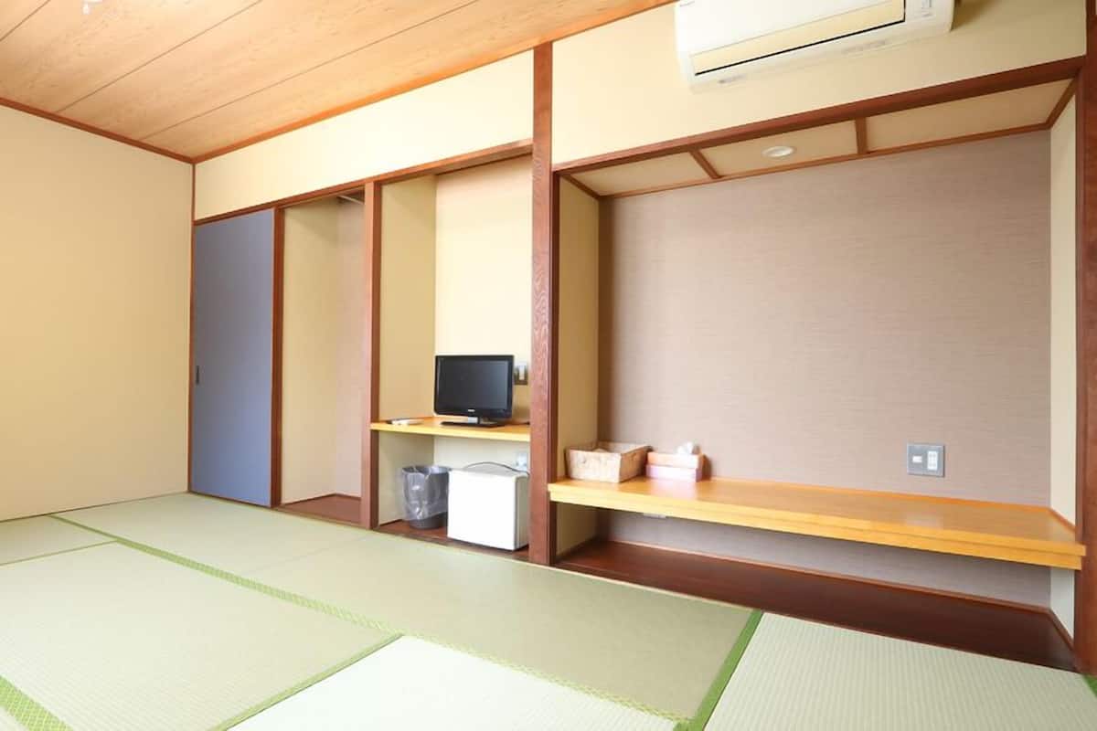 A room with tatami flooring, a television on a low shelf, and a small trash bin.