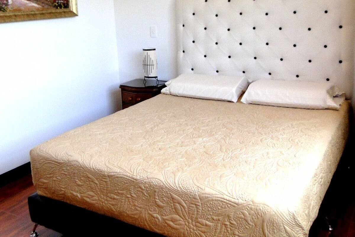 A neatly made bed with a tufted headboard, a bedside table with a lamp, and a framed painting on the wall.