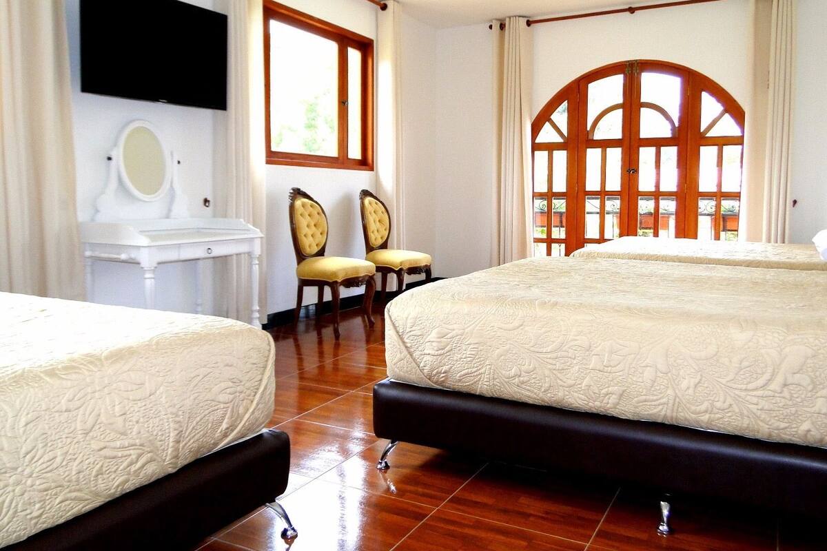 A hotel room with two beds, a vanity with a mirror, two chairs, and a large window with a view.