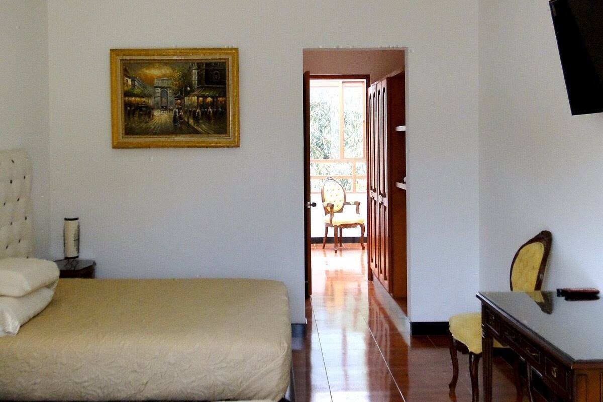 A hotel room with two beds, a desk, a chair, a painting on the wall, and a TV mounted on the wall.