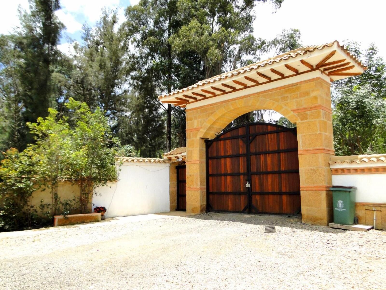 A gated entrance with a stone archway and a large wooden gate, surrounded by trees and a gravel driveway.
