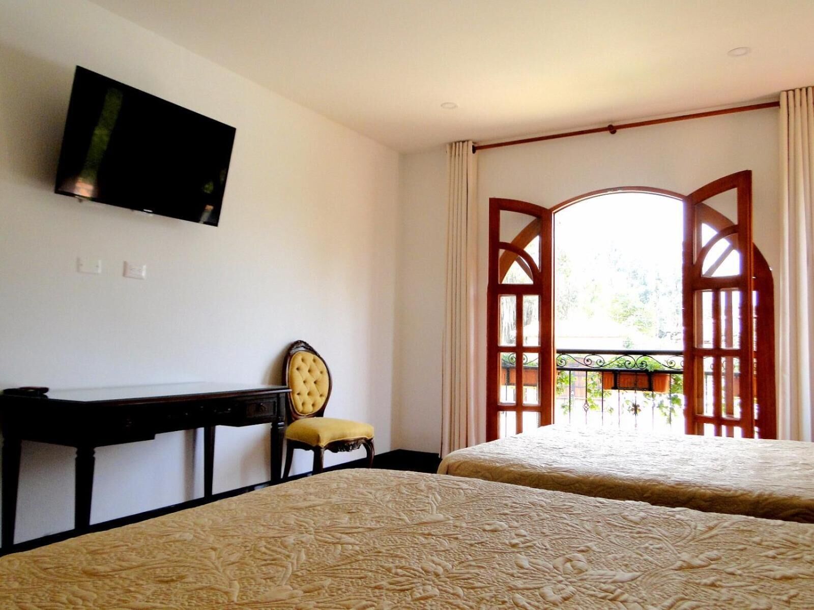 A hotel room with two beds, a TV mounted on the wall, a desk, and a chair.