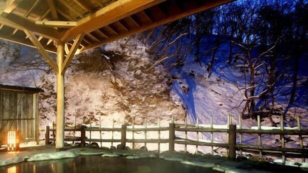 Une structure en bois surmontée d’un toit, entourée d’une clôture en bois, et dont l’image se reflète dans une étendue d’eau.