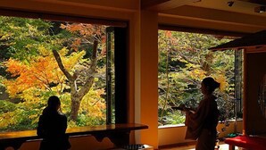 Une pièce de style japonais traditionnel, avec un sol recouvert de tatamis, une table basse et une grande fenêtre donnant sur un paysage automnal.