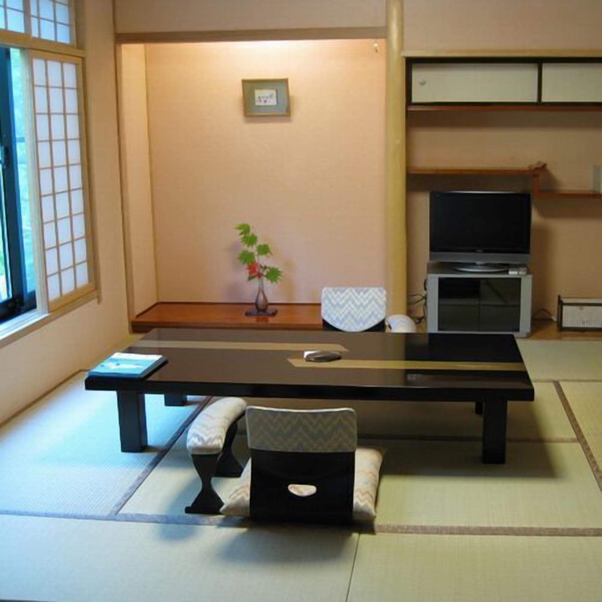 A tatami mat room with a low table, a chair, a small plant, a television, and a cabinet.