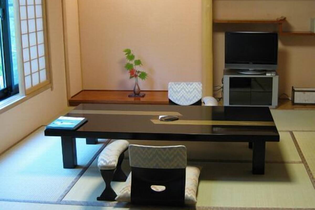 Ein Zimmer mit Tatami-Matten, einem niedrigen Tisch, einem Stuhl, einer kleinen Pflanze, einem Fernseher und einem Schrank.