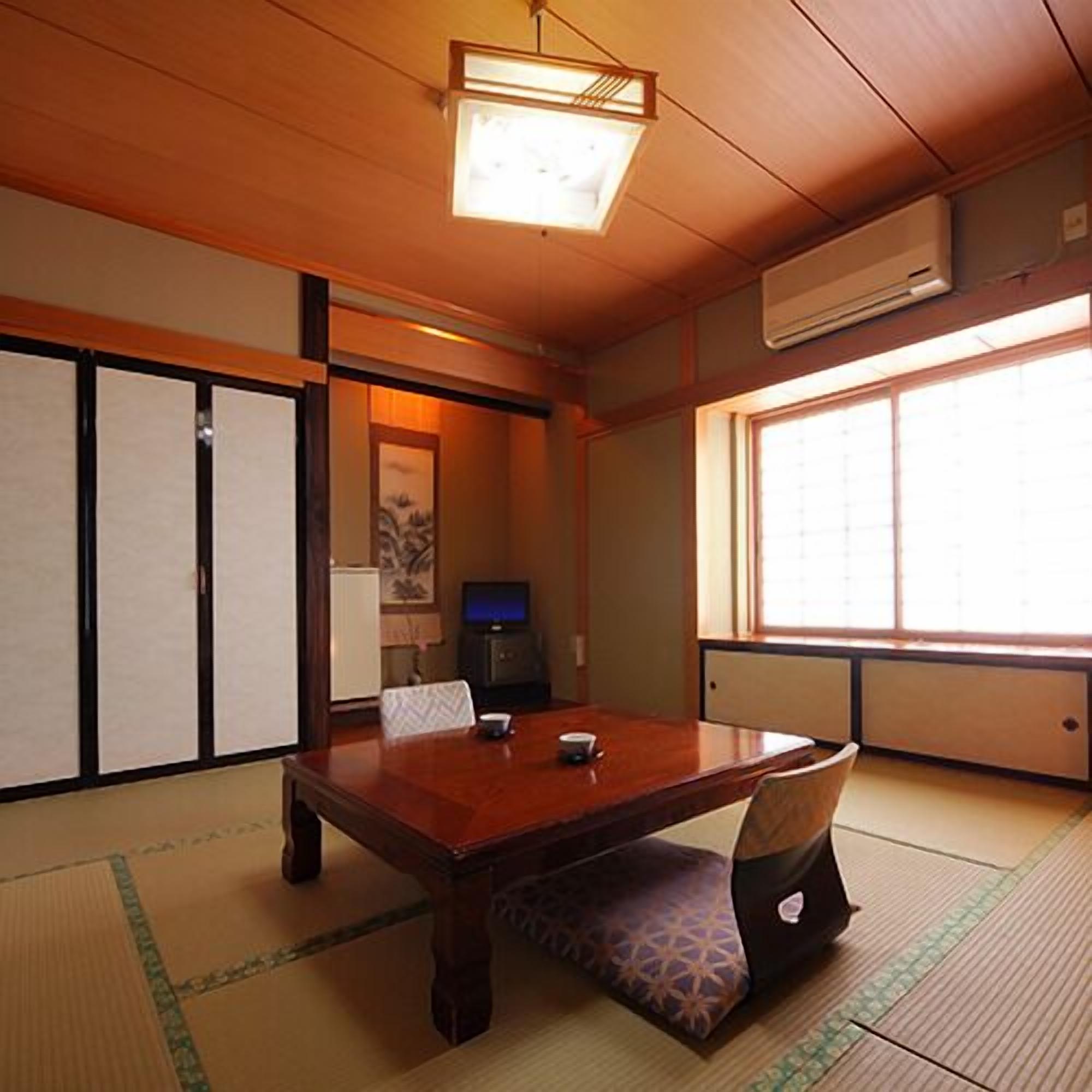 A traditional Japanese room with tatami flooring, a wooden table, a television, and sliding doors.