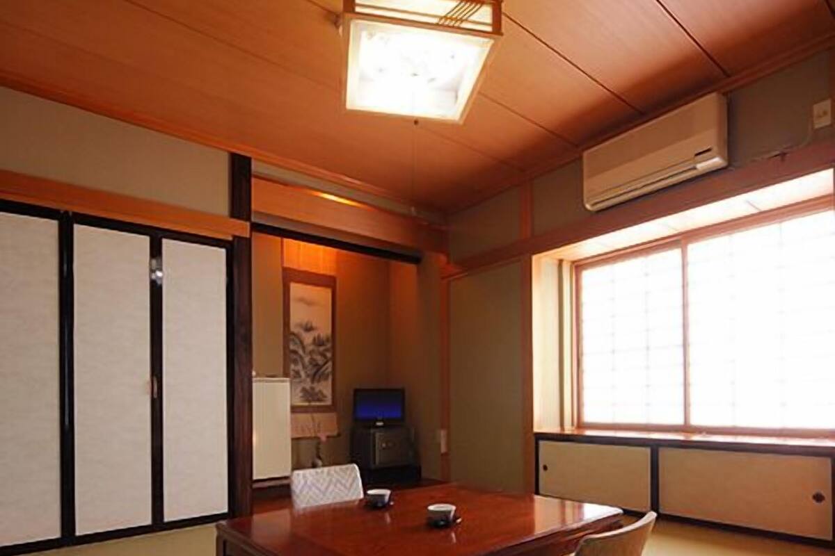 Ein traditioneller japanischer Raum mit Tatami-Böden, einem Holztisch, einem Fernseher und Schiebetüren.