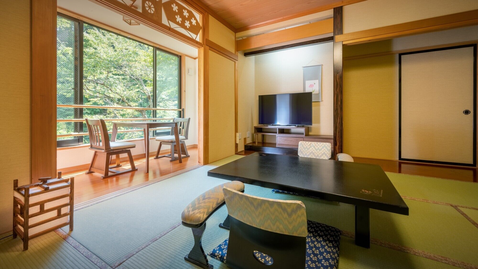 A traditional Japanese room with tatami flooring, a low table, chairs, a television, and a sliding door.