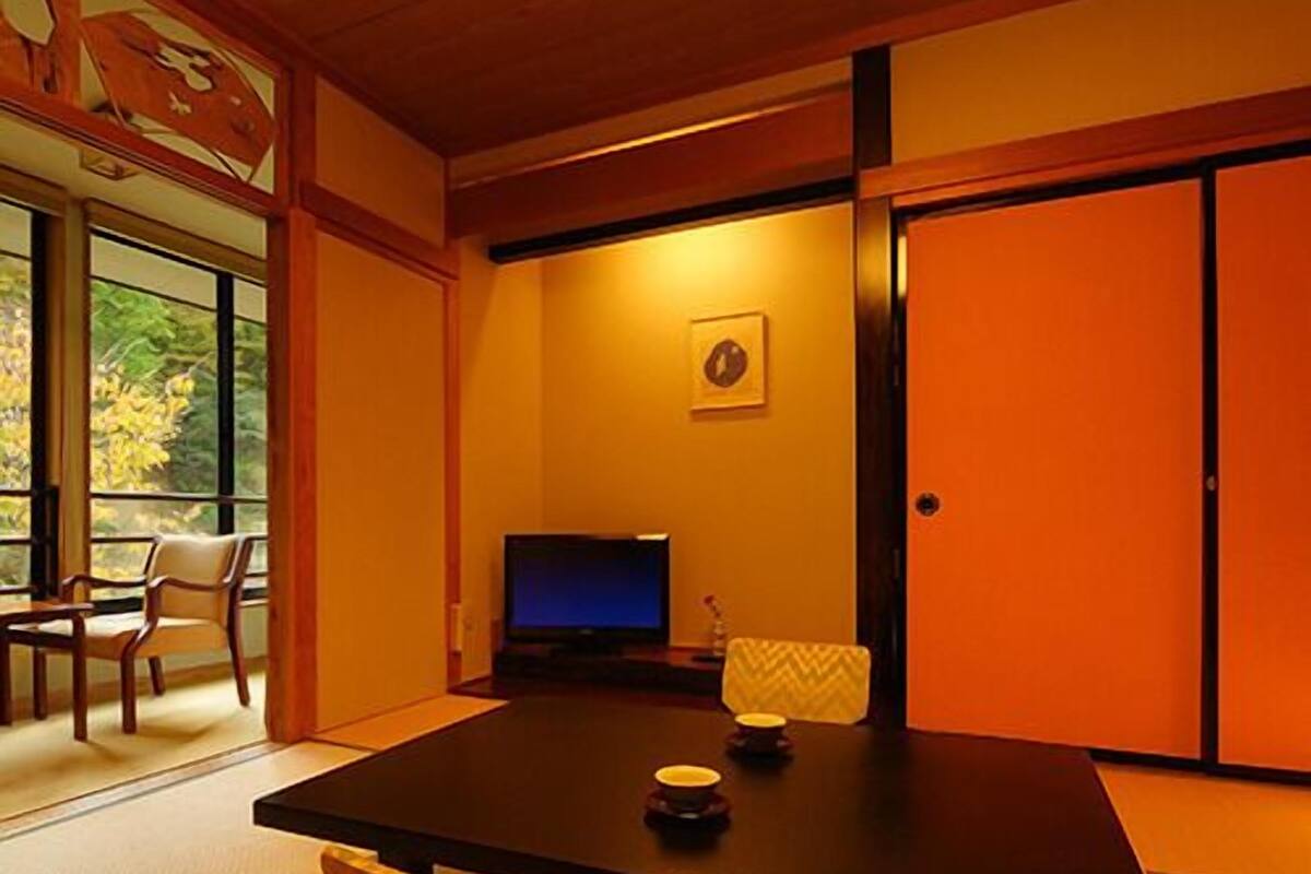 Ein traditioneller japanischer Raum mit Tatami-Boden, einem niedrigen Tisch, einem Fernseher und verschiebbaren Türen.