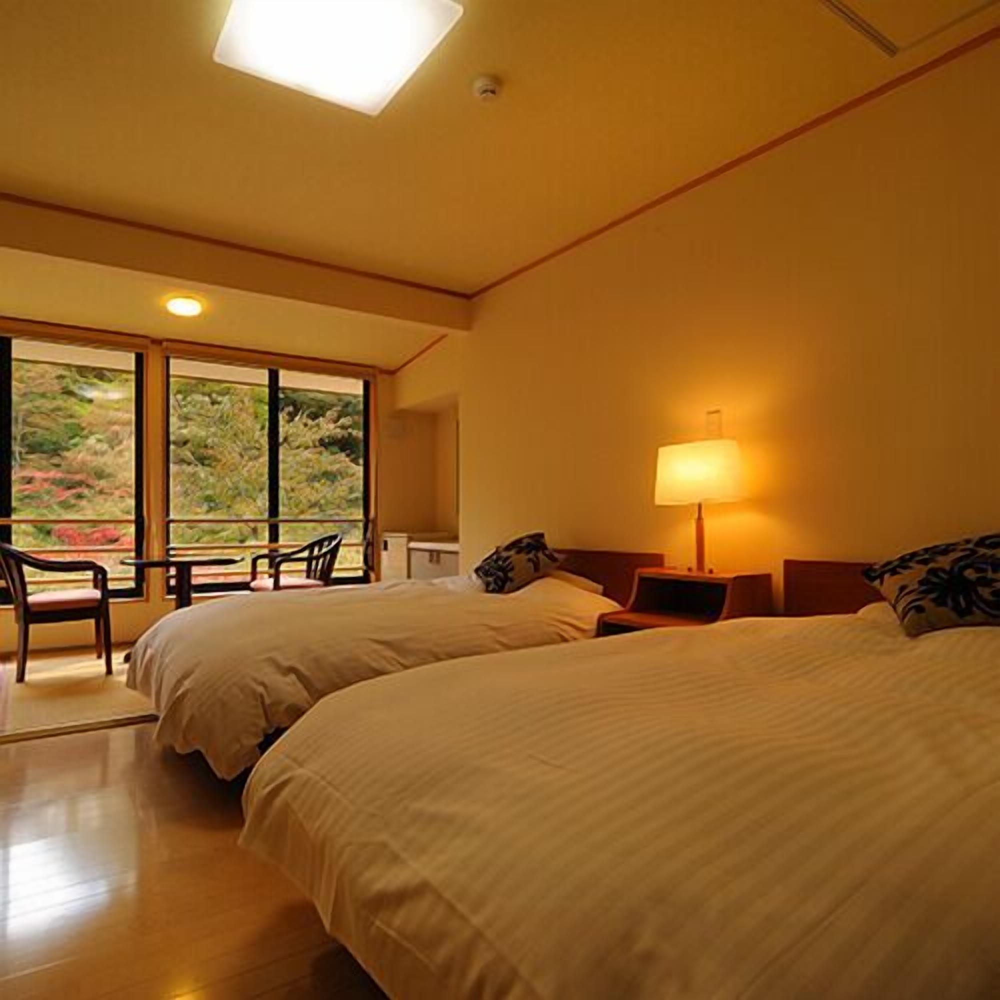 A hotel room with two beds, a nightstand, a lamp, a chair, and a large window with a view.