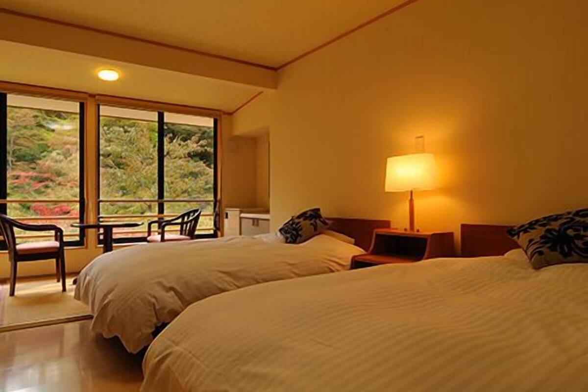 Ein Hotelzimmer mit zwei Betten, einem Nachttisch, einer Lampe, einem Sessel und einem großen Fenster mit Blick.