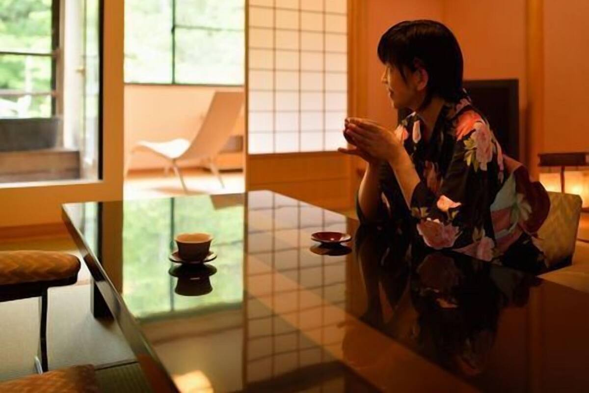 Ein traditioneller japanischer Raum mit Tatami-Böden, einem niedrigen Tisch und einer verschiebbaren Tür, die zu einem Garten führt.