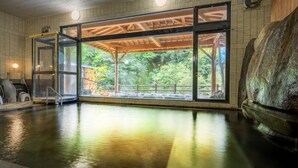 Un espace de bien-être doté d’une véranda en verre, d’une terrasse en bois et d’un grand rocher.