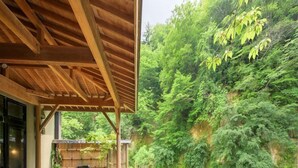 Une structure en bois avec un sentier de pierre menant à une source d’eau chaude, le tout entouré d’une végétation luxuriante et bordé par une rivière.