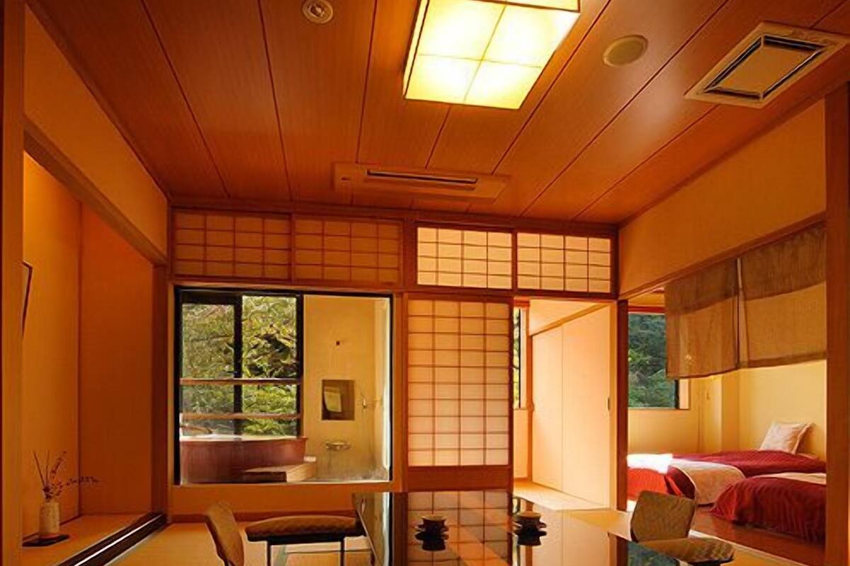Ein traditioneller japanischer Raum mit Tatami-Böden, einem niedrigen Tisch, einem Stuhl und einem Bett mit roter Bettwäsche.