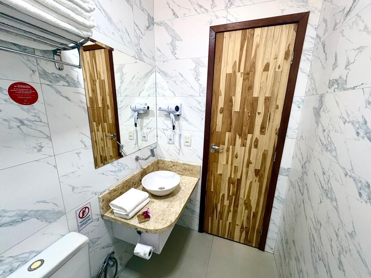 Une salle de bain avec un mur en marbre, un meuble-lavabo en bois, un évier et deux porte-serviettes.
