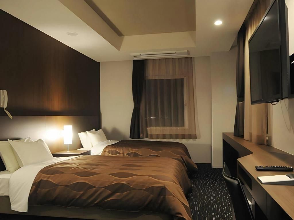 A hotel room with a bed, a desk, a chair, a television, and an air conditioning unit.