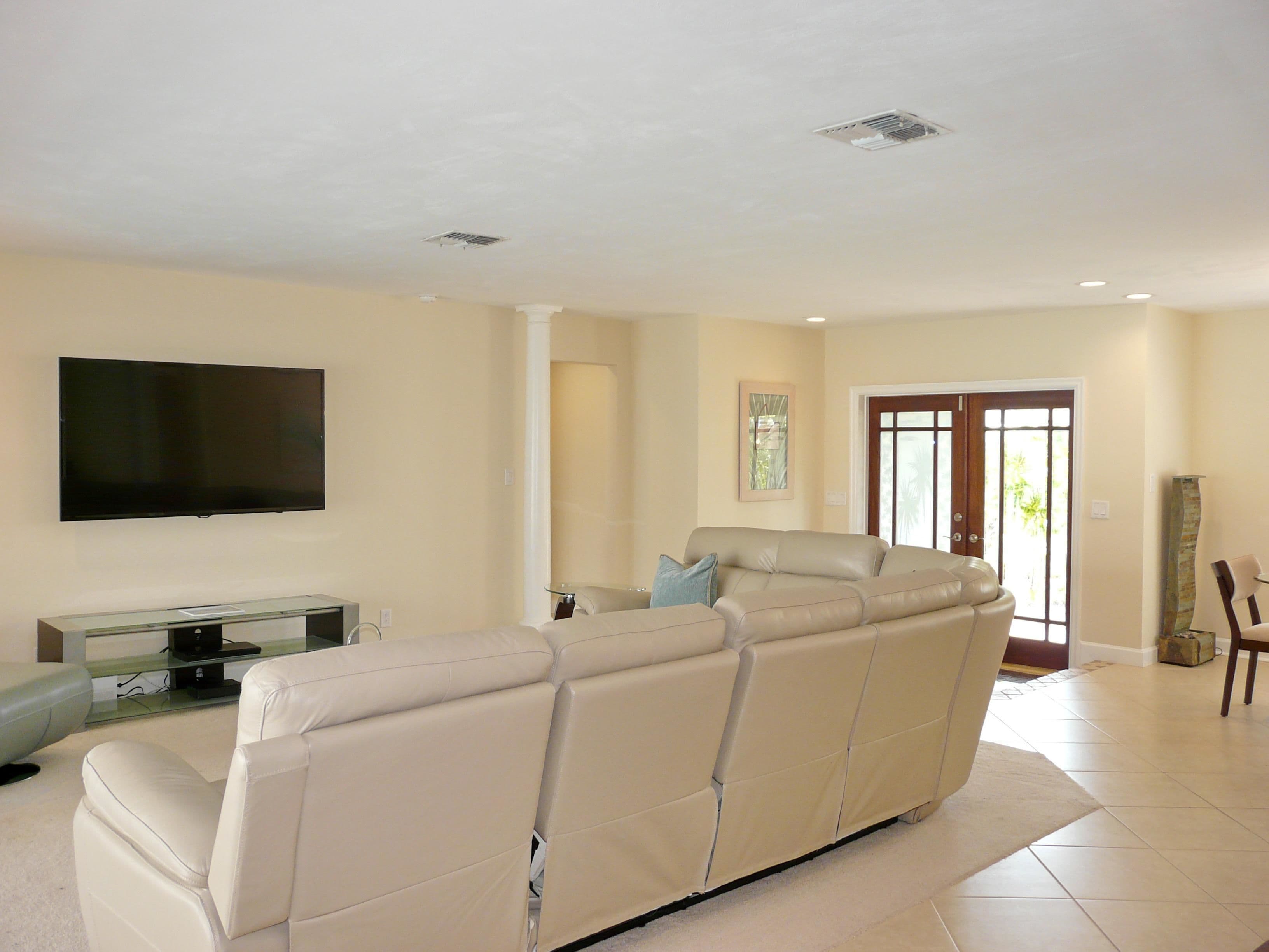 A living room with a large flat-screen TV, a beige leather sofa, and a glass coffee table.