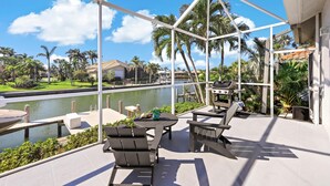 A covered outdoor patio with a view of a body of water, palm trees, and a distant building. - Relaxing Waterfront Home With Pool and Steps to Beach (Marco Island)