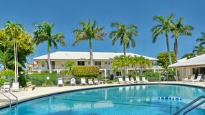 A swimming pool with lounge chairs and palm trees, surrounded by a building with a white roof. - Aquarius (Marco Island)