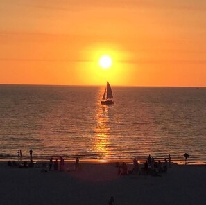 A sunset over a beach with a sailboat and people on the shore. - Seawinds (Marco Island)