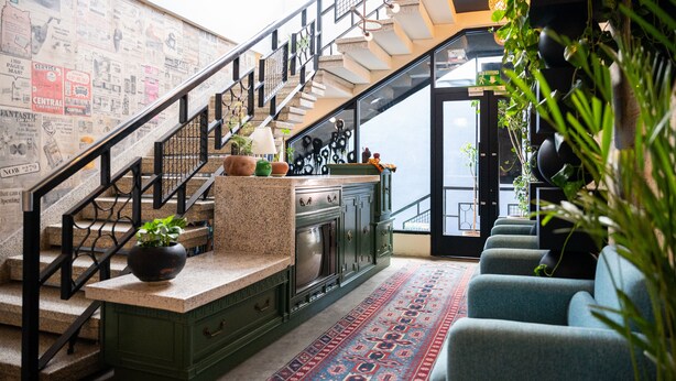 A staircase with a metal railing leading to a landing with a kitchen area, a seating area with blue chairs, and a wall covered with newspapers. - Hotel Boutique Lafayette Tijuana (Tijuana)