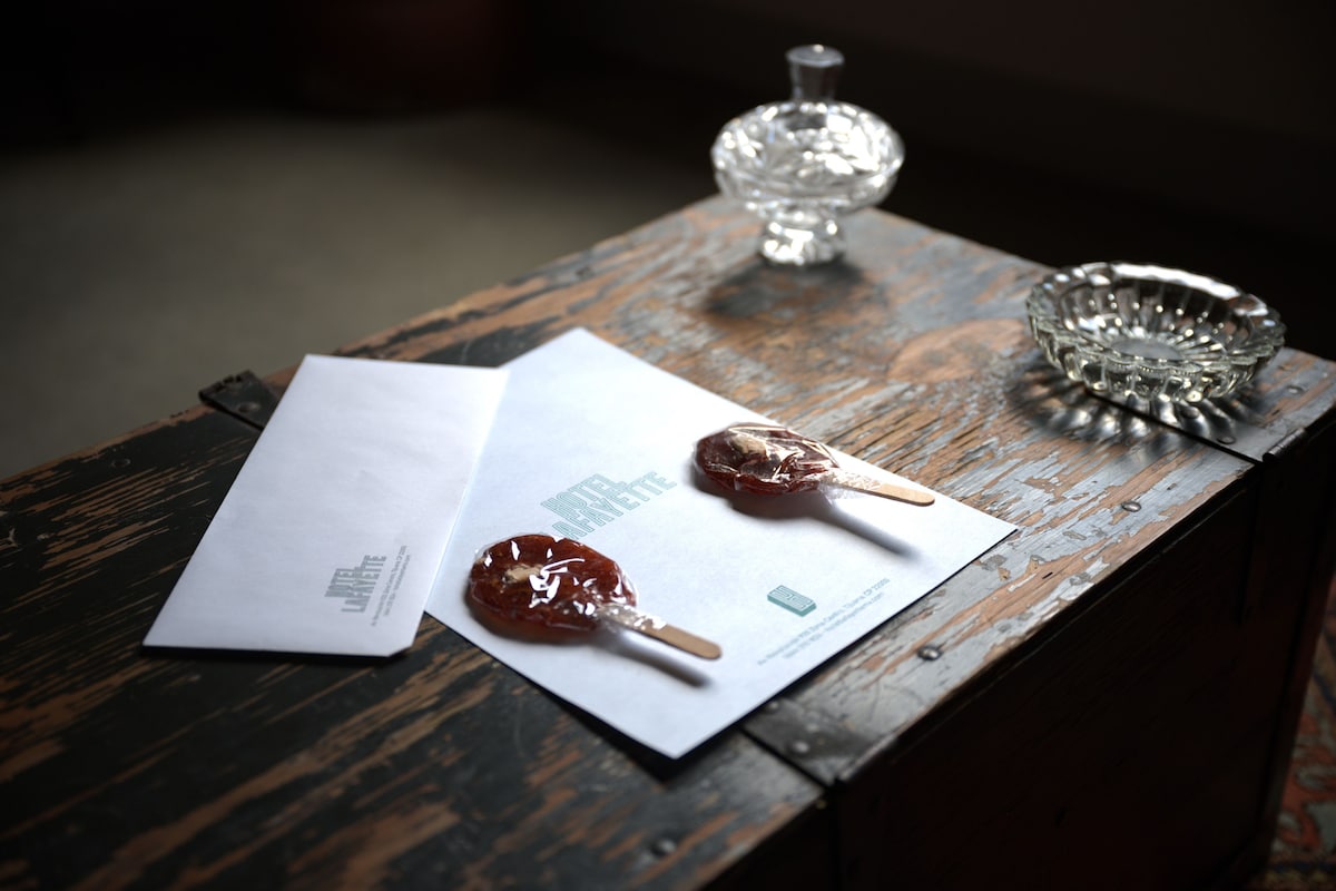 A wooden table with a white envelope, a lollipop, a crystal glass, and a metal ashtray.