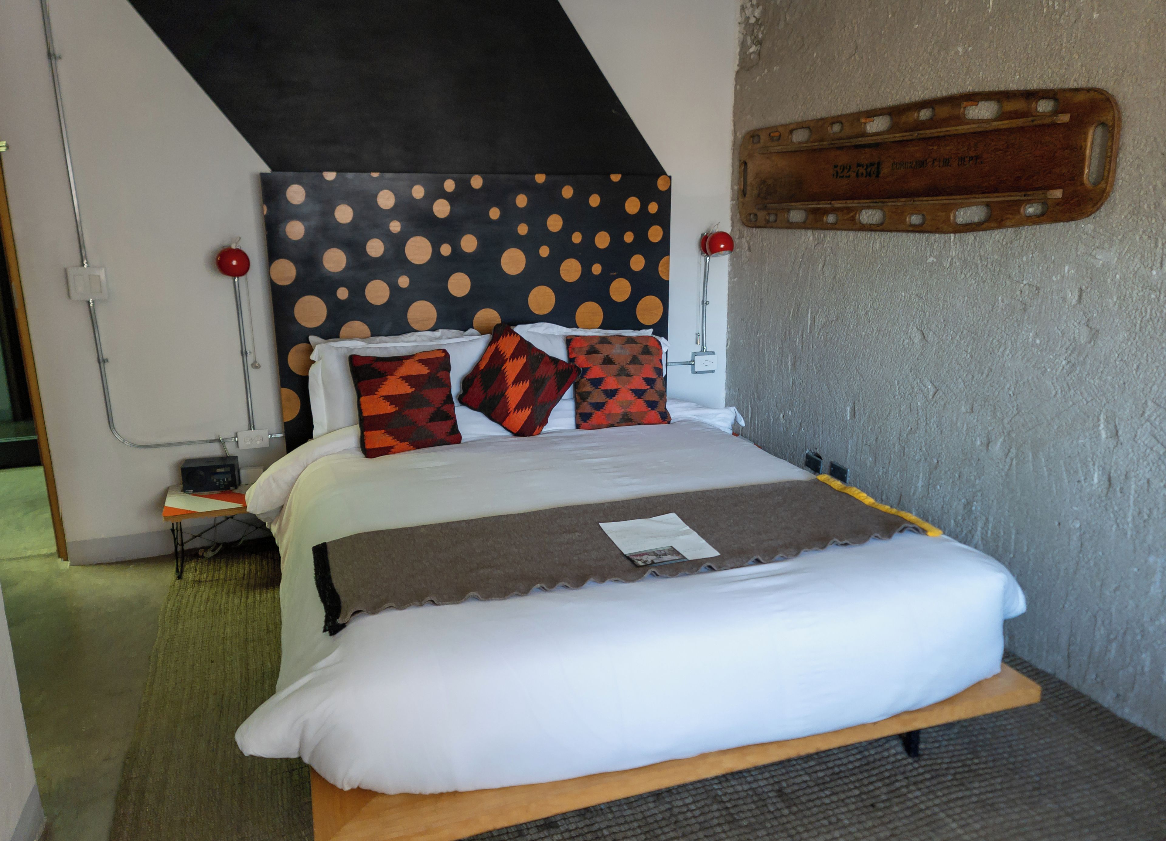 A neatly made bed with a patterned headboard, a bedside table with a radio, and a wall-mounted plaque.