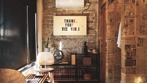 A cozy hotel room with a rustic brick wall, a patterned rug, a bed, a desk with a lamp, and a wall-mounted sign saying "THANK YOU! SEE YOU!". - Hotel Boutique Lafayette Tijuana (Tijuana)