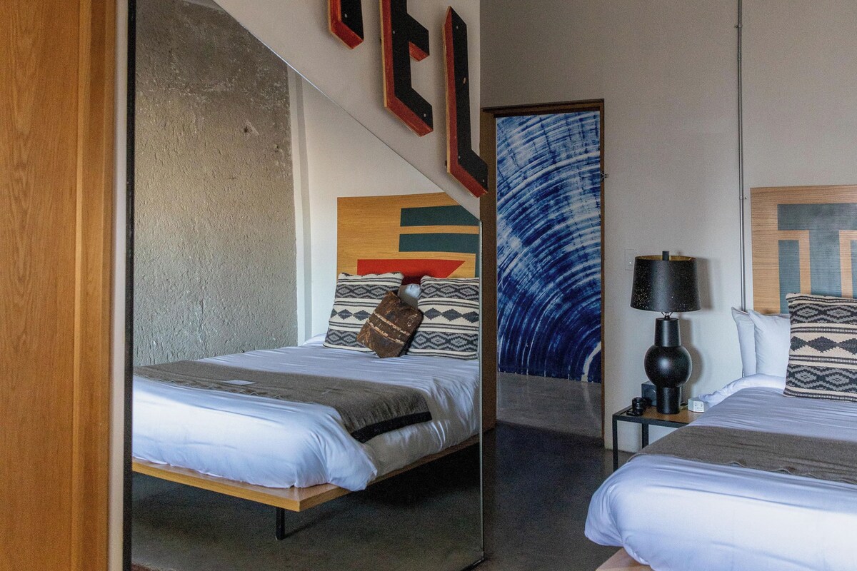 A hotel room with two beds, a large mirror, and a wall-mounted light fixture.