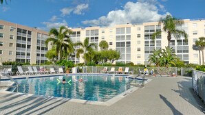 A swimming pool with lounge chairs, palm trees, and a multi-story building in the background. - Sands (Marco Island)