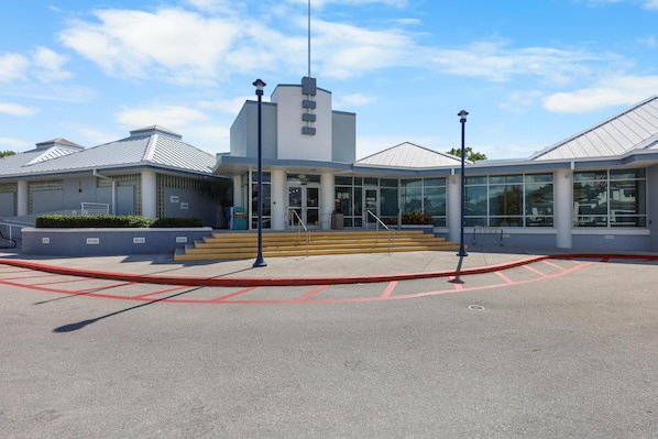 A modern building with a large glass entrance, steps leading up to the door, and a clear sky. - Inviting Condo With Pool Just a Steps From the Beach (Marco Island)