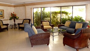 A spacious lobby with wicker furniture, a glass coffee table, and a large window offering a view of greenery. - Tradewinds (Marco Island)