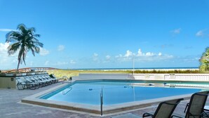 A rectangular pool with a clear view of the beach and ocean in the background. - Tradewinds (Marco Island)