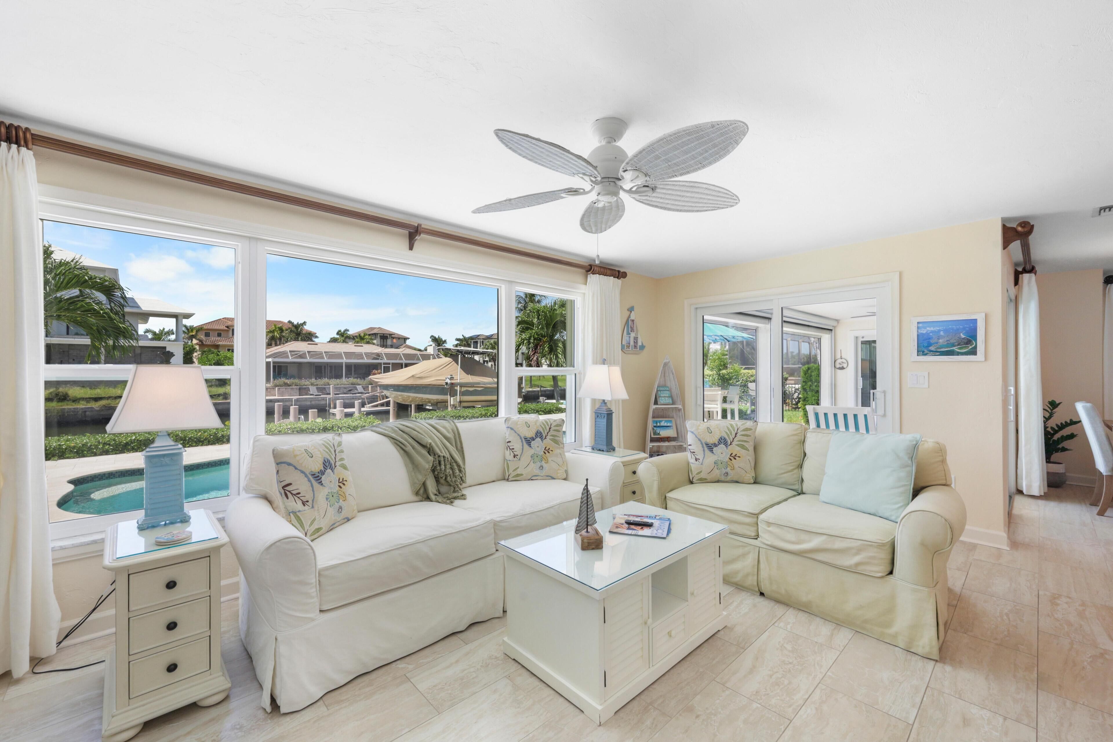 A spacious living room with a large window, a ceiling fan, and a pool view.